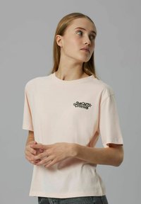 Kortärmad, ljusrosa t-shirt i bomull med rund halsringning och svart grafisk text på vänster bröst. Enkelt design och avslappnad passform.