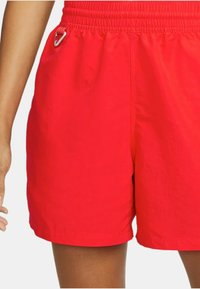 Röda, lätta shorts med elastisk midja, sidofickor och en liten metallklipp på vänster sida för att fästa föremål.