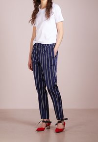 Bílá tričko spárované s námořnickými pruhovanými kalhotami. Kalhoty mají elastický pas a boční kapsy. Červené lodičky s špičatou špičkou a zapínáním kolem kotníku.