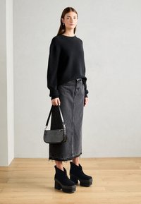 Pull noir en maille, jupe en denim gris avec ourlet effiloché, bottines noires à talons et petit sac à main noir à motif crocodile.