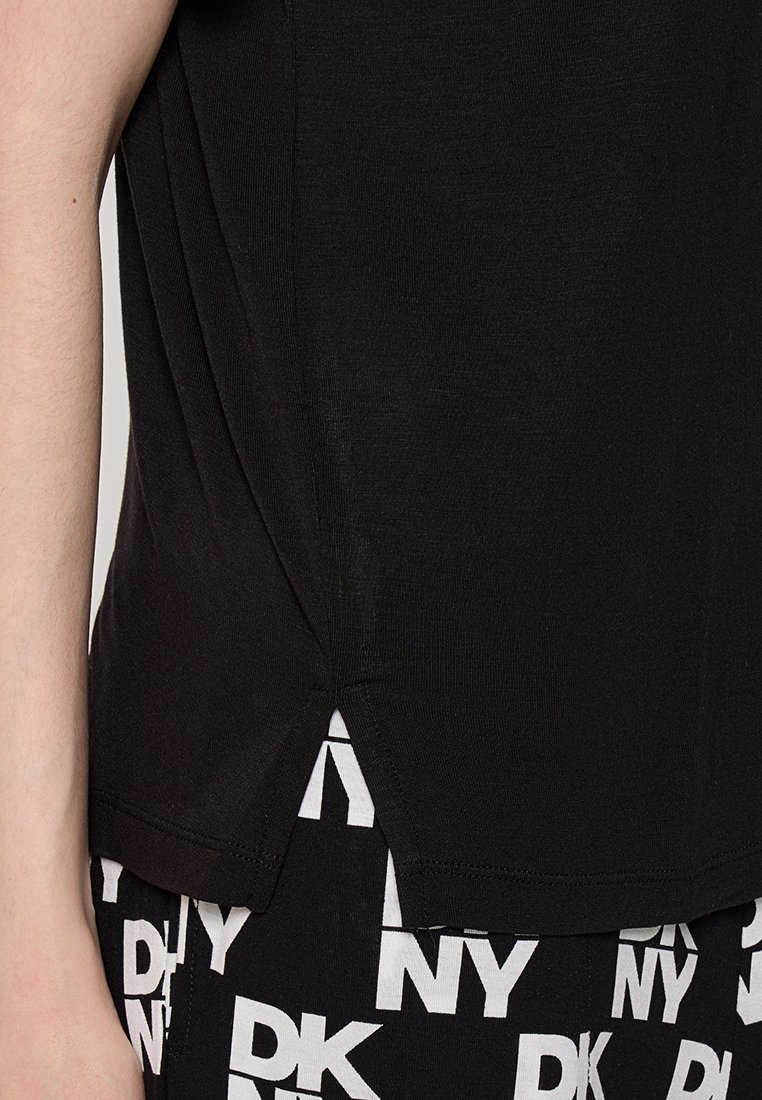 Czarna koszulka z krótkim rękawem z bocznym rozcięciem przy dolnym brzegu, wykonana z miękkiej bawełny. Widoczny biały wzór z literami na spodniach.