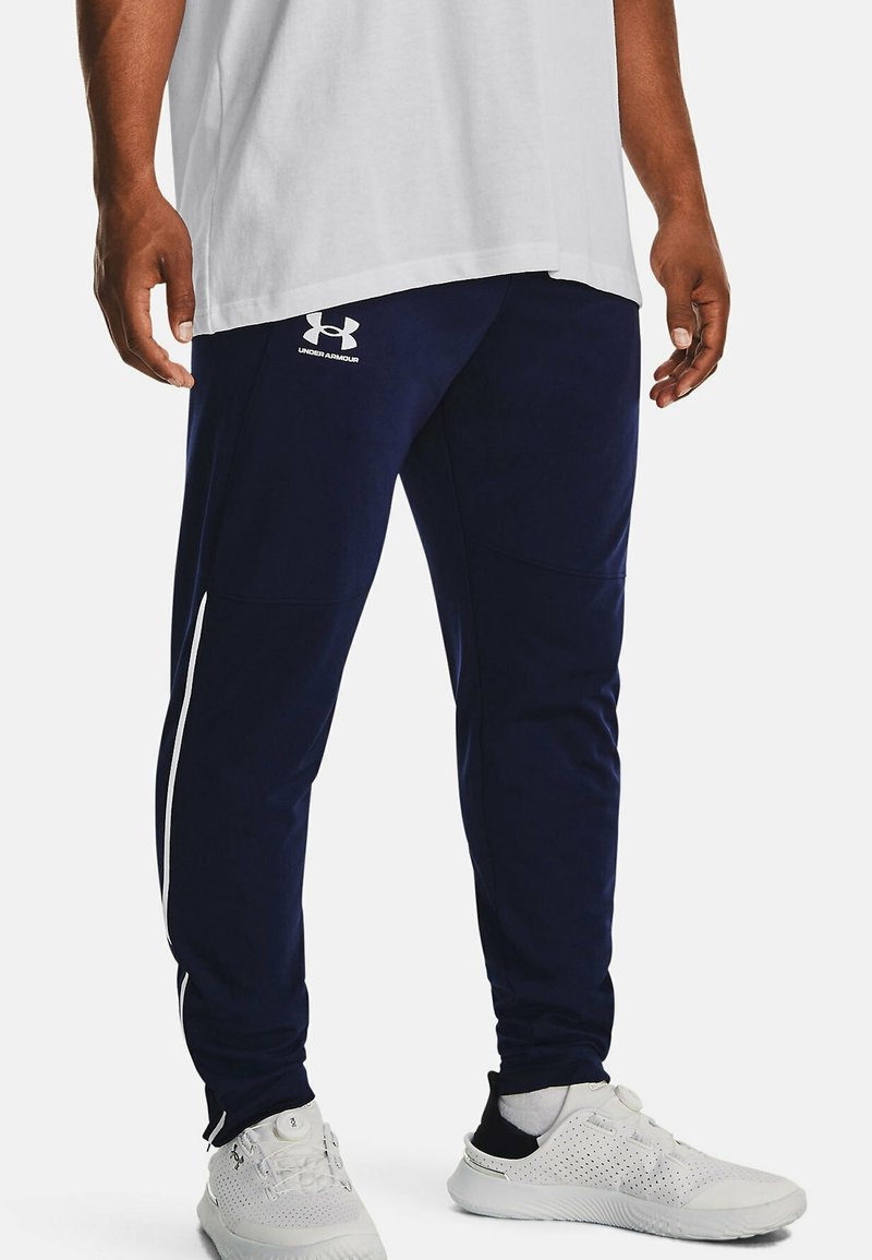 Námořnické sportovní kalhoty s bílými postranními pruhy, vyrobené z hladkého, elastického materiálu. Na levém stehně je logo Under Armour.