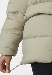 Giubbotto imbottito beige chiaro con design trapuntato, dotato di cordino ai polsini e texture liscia e morbida.