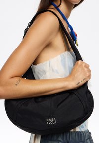 Czarna nylonowa torba na ramię o zaokrąglonym kształcie z zamknięciem na zamek. Posiada wytłoczone logo "BIMBA Y LOLA". Gładka faktura i minimalistyczny design.