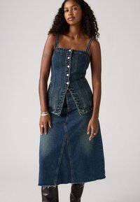 Tenue en denim comprenant un haut ajusté à boutons avec des coutures verticales et une jupe évasée jusqu'aux genoux avec une fente avant et un ourlet effiloché.