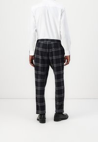 Schwarze und graue karierte Hose mit elastischem Bund, Gesäßtasche und schmaler Passform, kombiniert mit einem weißen Langarmshirt.