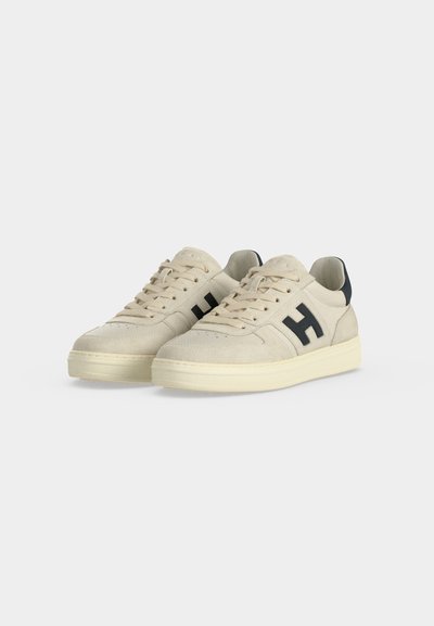 Paire de baskets basses beiges avec semelles crème, lacets beiges et logo noir "H" sur le côté, présentées sur fond blanc.