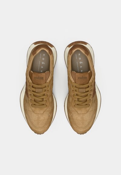 Brūnas zamšādas sporta kurpes ar teksturētu apdari, apaļu purngalu un kontrastējošām baltām zolēm. Aprīkotas ar plānām šņorēm un logotipu uz mēles.