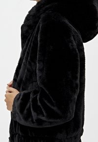 Black faux fur jacket with a zip closure, hood, and ribbed cuffs. The fabric has a soft, textured surface with subtle sheen.