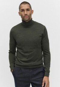 Groene coltrui van zachte stof, met lange mouwen en een snug fit, gecombineerd met donkere broeken. Eenvoudige, geribbelde accenten.