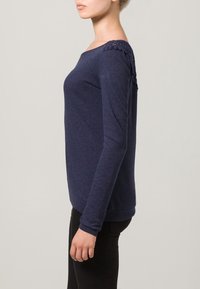 Marineblauw top met lange mouwen en een gestructureerd schouderdetail. Gemaakt van zachte stof, met een ontspannen pasvorm en een afgeronde halslijn.