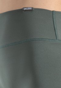 Zielone oliwkowe legginsy do jogi z wysokim stanem, charakteryzujące się gładką teksturą, płaskimi szwami oraz małą metką marki na pasku.