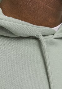 Sudadera verde menta con un tejido texturizado, que presenta un cordón en el escote. Enfocándose en el suave punto y en los sutiles detalles de costura.
