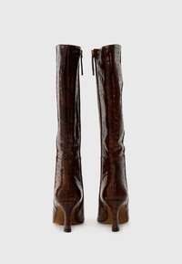 Bottes hautes en cuir synthétique marron avec une conception ajustée, des talons effilés et des fermetures éclair à l'arrière. La texture lisse et la finition brillante mettent en valeur les détails.