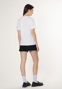 Hvid T-shirt med korte ærmer og rund halsudskæring, parret med sorte shorts. Outfittet har en afslappet pasform og en glat tekstur.