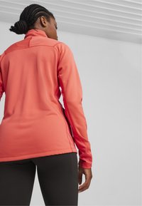 Getailleerde, lang mouw atletische top in levendig koraal, met gestructureerde stof, een hoge kraag en contrasterende naden, gecombineerd met zwarte leggings.