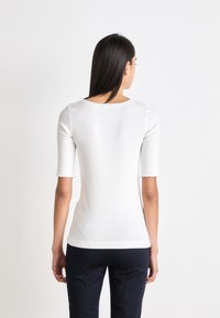Top bianco a maniche corte con scollatura rotonda e design aderente, realizzato in tessuto liscio, abbinato a pantaloni scuri, visto da dietro.