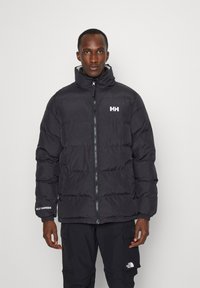 Zwarte pufferjack met hoge kraag, frontale rits en geborduurd logo. Beschikt over horizontaal gestikte secties voor isolatie. Te combineren met zwarte broek.