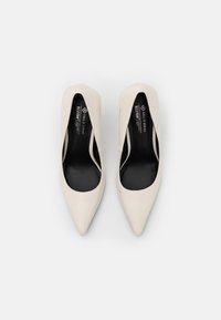 Beige højhælede pumps med spidse tå, glat læderoverdel og sort indre foring. Minimalistisk design uden synlig hardware.