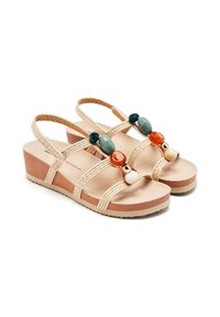 Sandalias de cuña beige con correas trenzadas. Presentan cuentas decorativas coloridas en verde, azul, naranja y crema en la parte delantera. Suela suave.