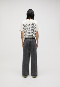 Cream t-shirt featuring black text "marimekko" in varying sizes. Wide-leg dark jeans with floral pattern. Green sole shoes.