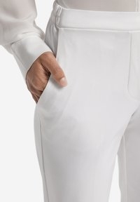 Vita skräddarsydda byxor med elastisk midja och sidofickor, tillverkade av ett slätt tyg med en viss lyster.