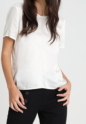 Biały top z krótkim rękawem wykonany z gładkiej tkaniny, z okrągłym dekoltem i luźną sylwetką, w połączeniu z czarnymi, dopasowanymi spodniami z okrągłymi guzikami.