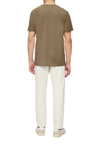 Brązowa bawełniana koszulka z okrągłym dekoltem, krótkimi rękawami i luźnym krojem. W połączeniu z białymi bawełnianymi spodniami i casualowymi trampkami.