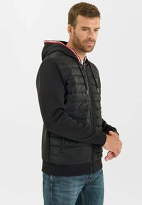 Svart vadderad hoodie med ribbade muddar och nederkant, med dragkedja framtill, kontrasterande röd och vit huva, samt sidofickor.