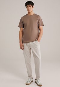 Maglietta corta marrone a maniche corte, pantaloni leggeri a righe e sneakers bianche con dettagli verdi. Design semplice e vestibilità rilassata.