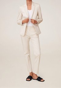 Blazer beige sur mesure, pantalon slim assorti et sandales tissées noires. Le tissu semble lisse avec une coupe structurée et des lignes nettes.