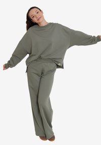 Oversized oliwkowy sweter i pasujące spodnie, wykonane z miękkiego materiału, cechujące się luźnym krojem, długimi rękawami i szerokimi nogawkami.