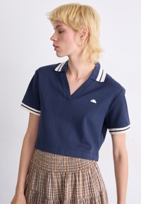 Navy polo shirt with a V-neck and short sleeves, featuring white and navy striped accents on the collar and sleeves. Small logo detail on chest.