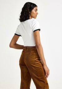 Witte shirt met korte mouwen en marineblauwe afwerking, gecombineerd met high-waisted bruine corduroy broek met rechte pijpen en achterzakken.