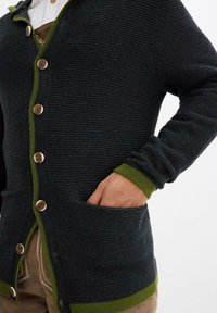 Cardigan scuro a coste con dettagli verdi, con scollo a V, chiusure a bottone e tasche frontali. Il materiale è testurizzato e lavorato a maglia.