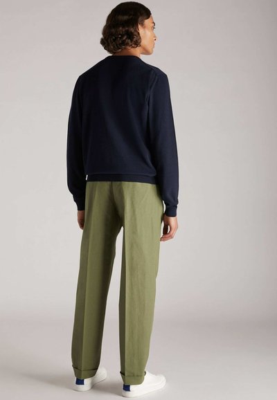 Marineblaues Sweatshirt mit gerippten Bündchen, kombiniert mit olivgrünen weit geschnittenen Hosen und weißen Sneakers. Glattes Material und lässiger Schnitt.