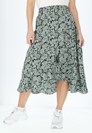 Jupe florale avec un fond noir et des motifs floraux verts, une silhouette fluide et une taille élastique. Portée avec des baskets blanches.