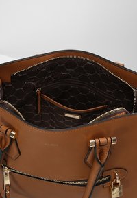 Brązowa skórzana torba na ramię z złotymi akcentami, zamknięcie na zamek błyskawiczny i podszewka z logo; posiada wiele kieszeni do organizacji.