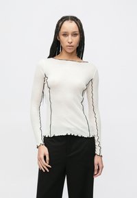 Bluză albă cu mâneci lungi, cu dantelă neagră ondulată de-a lungul decolteului și manșetelor, confecționată dintr-un material ușor. Design fără cusături.