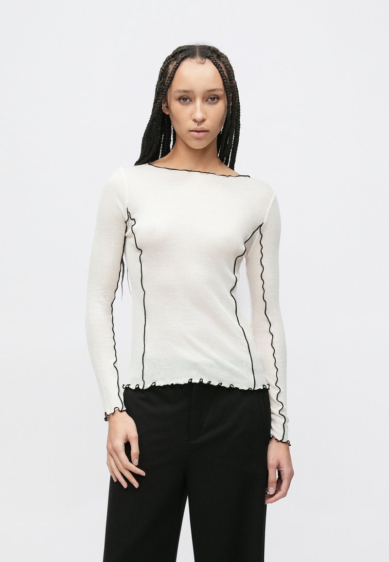 Bluză albă cu mâneci lungi, cu dantelă neagră ondulată de-a lungul decolteului și manșetelor, confecționată dintr-un material ușor. Design fără cusături.