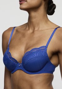 Blauwe kanten beha met beugel, met geschulpte kanten randen, satijnen bandjes en een decoratief metalen accent in het midden.