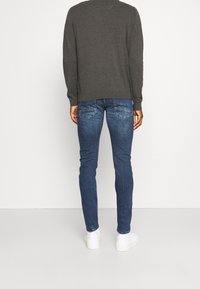 Pull gris foncé, jean bleu slim et baskets blanches. Le jean comporte des poches arrière avec des surpiqûres décoratives. Design simple, look contemporain.