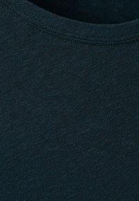 Gros plan sur un tissu en coton bleu marine foncé montrant une texture fine de tricot et un détail de couture de l'encolure ronde.
