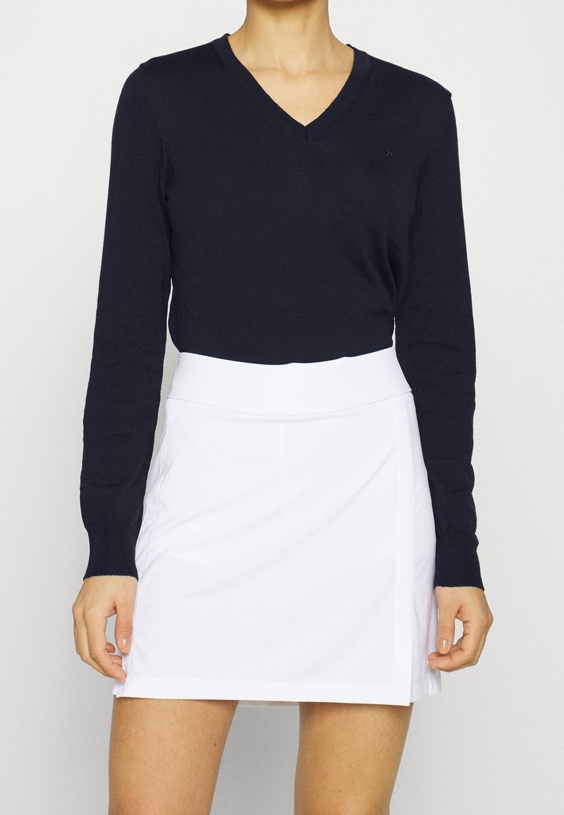 Navy V-Ausschnitt Langarm-Strickoberteil, kombiniert mit einem weißen plissierten Minirock. Das Outfit verfügt über einen taillierten Bund und eine glatte Stofftextur.