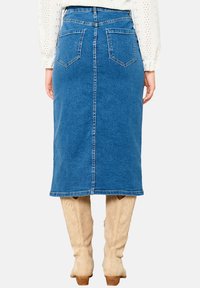 Denim midi krilo v srednje modri barvi, v obliki A, z dvema zadnjima žepoma, šivanimi šivi in ravnim robom, noseno z kremnimi škornji do kolen.