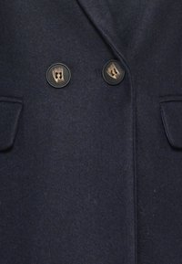 Czarnoniebieski wełniany płaszcz z dwoma dużymi ciemnymi guzikami i dwiema klapkowymi kieszeniami z przodu.