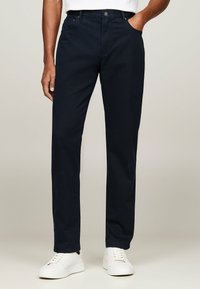 Chino blu navy realizzati in misto cotone, con taglio diritto, tasche laterali e chiusura con bottone. Abbinati a sneaker bianche.