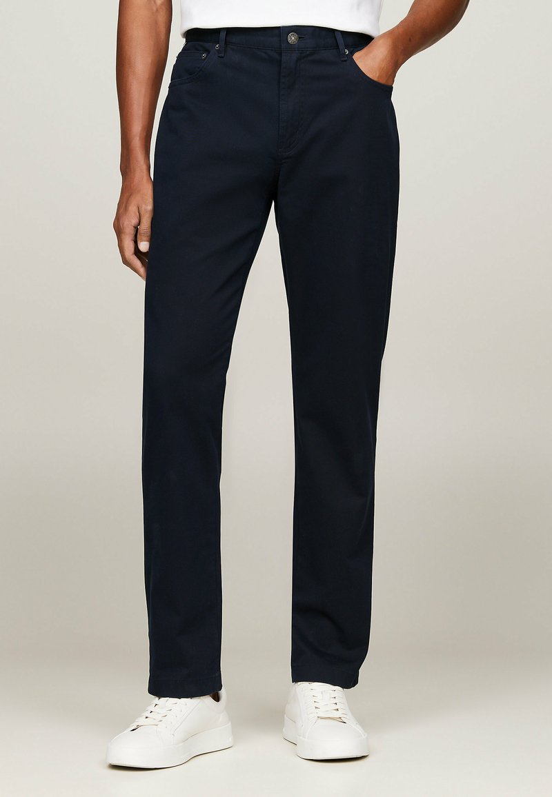 Chino blu navy realizzati in misto cotone, con taglio diritto, tasche laterali e chiusura con bottone. Abbinati a sneaker bianche.