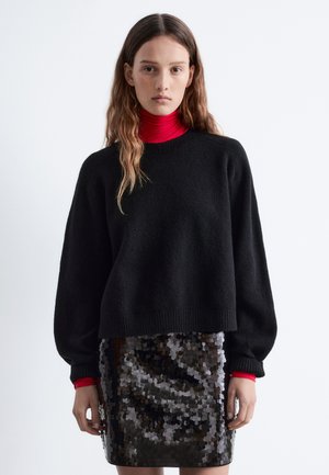 Black knitted sweater with a loose fit and ribbed cuffs, layered over a fitted red turtleneck, paired with a shiny black sequined skirt.