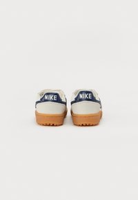 Nike sneakers met een crèmekleurige bovenkant en marineblauwe accenten, een gladde textuur en een gumrubberen buitenzool. Inclusief branding op de hak.